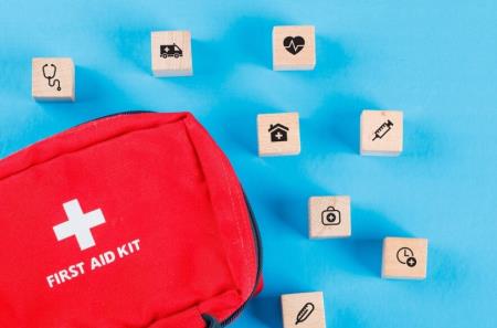 Flatlay photograph of red first aid kit bag, with wooden blocks on a blue background